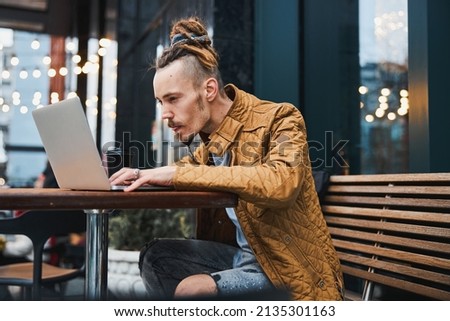 Young trendy man typing on laptop outdoors