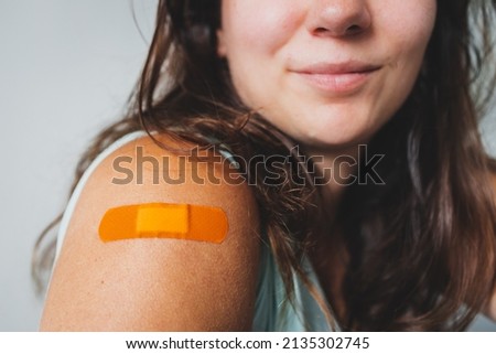 woman showing covid-19 vaccination band-aid on her arm, concept of protection from the pandemic and coronavirus health risks Royalty-Free Stock Photo #2135302745