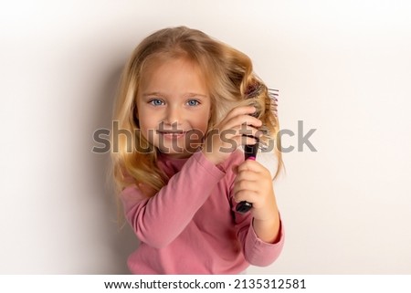A pretty little girl with big blue eyes and a comb in her hand. The child combs unruly hair. Cute little girl is playing with a hairbrush. Royalty-Free Stock Photo #2135312581