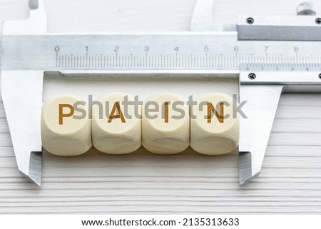 Pain rating scales, clinical concept : Vernier caliper measures wood cubes with the word PAIN, depicting an unpleasant sensory or emotional experience, and for experiencing pain consciously. Royalty-Free Stock Photo #2135313633