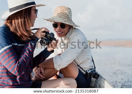 Male and female Asian tourist photographers having fun chatting and view photos in the camera.