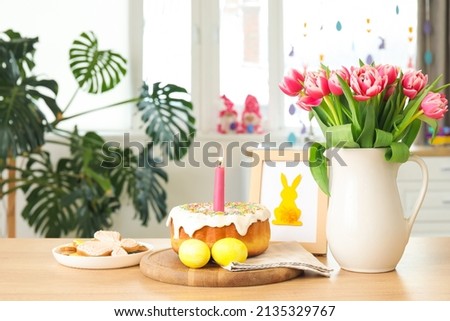 Easter cake, candle, eggs, cookies, picture and vase with tulips on counter in kitchen