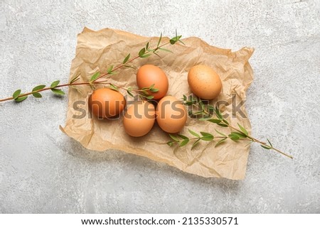 Parchment with Easter eggs and green leaves on light background