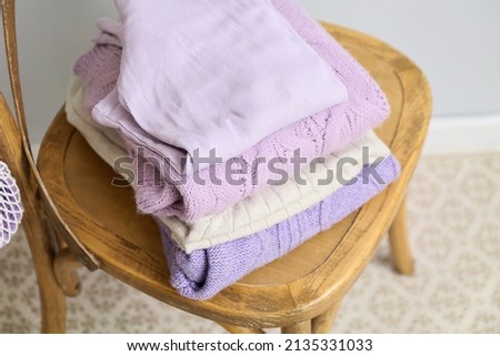 Stack of knitted sweaters on chair near light wall, closeup