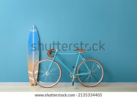 Bicycle and surfboard near color wall in room Royalty-Free Stock Photo #2135334405