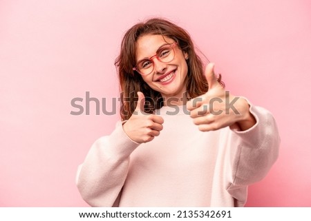 Young caucasian woman isolated on pink background raising both thumbs up, smiling and confident.