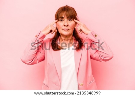 Middle age caucasian woman isolated on pink background focused on a task, keeping forefingers pointing head.