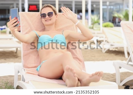 Young blonde woman lay on sunbed, wave hi to friend on video call