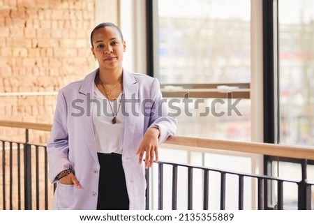 Portrait of confident multiracial LGBTQ mid adult woman leaning on railing in modern office space Royalty-Free Stock Photo #2135355889