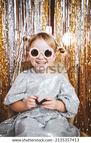Portrait of happy little girl in dress and sunglasses having fun on the festive background. Kids birthday or fancy dress party, disco music or New Year. Celebration and Holiday concept.