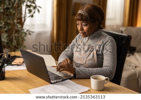 A young woman works at a desk in her office. There are papers lying next to her. The young woman plans the new week on a calendar. Work organization. Working at home.