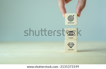 Mission, vision and values of company. Purpose business concept. Hand holds wooden cube with mission vision and values symbols on grey background. Modern vertical design. Business presentation. Banner Royalty-Free Stock Photo #2135373199