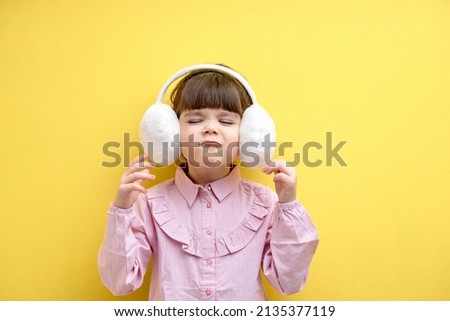 Funny child girl in blouse listen to music in headphones and dance, wearing big wireless headset isolated on yellow studio background