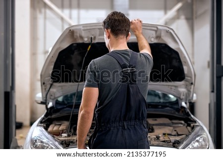 professional car mechanic working under car hood in repair garage, closing or opening the hood, working alone. car service, repair, maintenance and people concept. at modern clean workshop. rear view Royalty-Free Stock Photo #2135377195