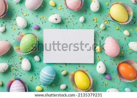 Top view photo of easter decorations paper sheet multicolored easter eggs in paper baking molds and confectionery topping on isolated teal background with blank space