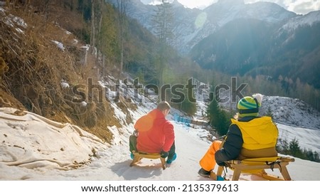 Father and son, sledding on wooden sleds from the top of the snowy slope