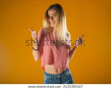 Sporty lovely girl in tank-top and denim shorts dancing with pleasure and smiling. Indoor portrait of stunning female model with vintage hairstyle waving hands on yellow background.