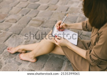 Cropped photo of a woman in dress with a pensil writing in a notebook