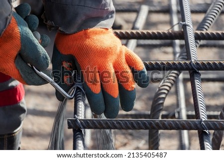 A worker uses steel tying wire to fasten steel rods to reinforcement bars. Close-up. Reinforced concrete structures - knitting of a metal reinforcing cage
