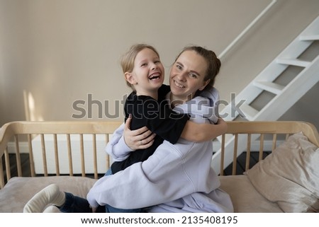 A happy family, mom and daughter hugging and smiling, sitting on the couch in the room, looking at the camera. Mother's Day.