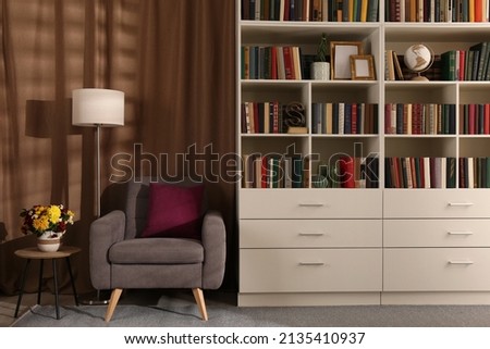 Cozy home library interior with comfortable armchair, floor lamp and collection of books on shelves Royalty-Free Stock Photo #2135410937