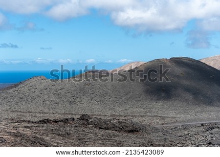 Desértic landscape with light sand and mointains and a blue sea at the back on a Sunny sumer day with blue Sky and some clouds on Lanzarote canary islands
