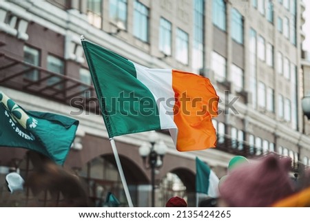 National Flag of Ireland close-up above people crowd, city street, traditional carnival of St. Patrick's Day