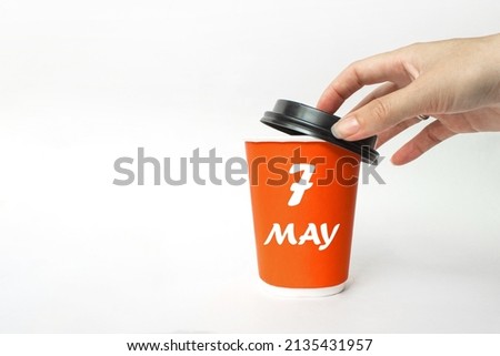 May 7th. Day 7 of month, Calendar date. A woman's hand open black plastic cap of red disposable cardboard  coffee paper cup with Calendar Date. Spring month, day of the year concept