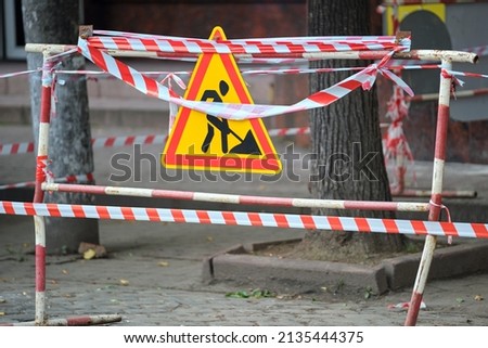 Warning roadworks sign and safety barrier on city street during maintenance repair work