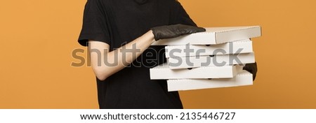 Pizza delivery man, a man in a black T-shirt and gloves with boxes in his hands on a yellow background, close-up