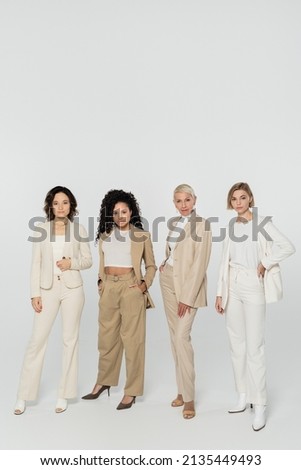 Multiethnic businesswomen posing and looking at camera on grey background