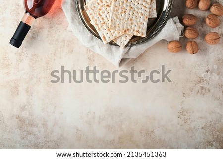 Passover celebration concept. Matzah, red kosher and walnut. Traditional ritual Jewish bread on sand color old concrete background. Passover food. Pesach Jewish holiday.  Royalty-Free Stock Photo #2135451363