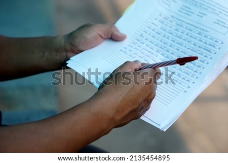 Closeup teacher's hand holds pen to check and correct paper test. Concept : Education evaluation. Writing test. Student's essay, research proposal.         