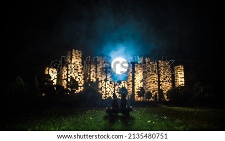 Cartoon style city buildings. Realistic city building miniatures with lights. background. Romantic couple sitting in from of nigth city in selective focus
