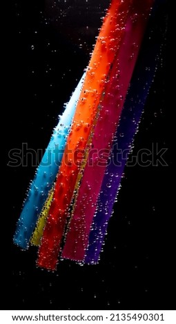multicolored sticks under water with a trail of transparent bubbles.