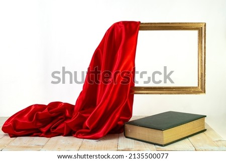 golden frame unveiled by a red satin curtain over a green thick book
