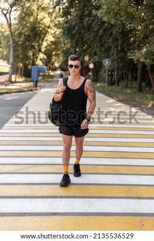 Cool athletic guy with sunglasses in summer style clothes with a backpack goes to practice crosswalk
