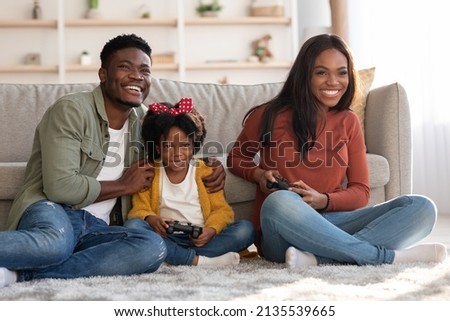 Family Pastime. Cheerful Black Parents Playing Video Games With Little Daughter At Home, Happy African American Mom, Dad And Female Child Using Joysticks And Having Fun Together, Free Space Royalty-Free Stock Photo #2135539665