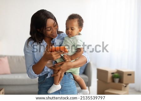 Babysitting. Portrait of African American woman holding baby on hands and showing her son pictures on phone screen, mother and child watching cartoons or making video call with grandparents