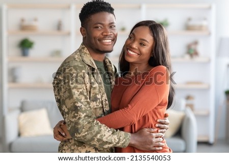 Portrait Of Young African American Male Soldier And His Wife Hugging At Home, African American Military Man Wearing Camouflage Uniform Embracing His Spouse And Smiling At Camera, Copy Space