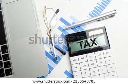 tax text on calculator screen, glasses, laptop and charts. High quality photo