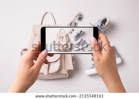 Woman taking photo of white leather backpack, pastel blue sneakers and sunglasses with smartphone. Blogger, influencer or stylist capturing spring fashion accessories for social media.