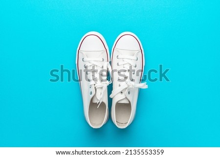 Minimalist flat lay image of white gumshoes over turquoise blue background with copy space. Flat lay top-down composition of pair of white sneakers.