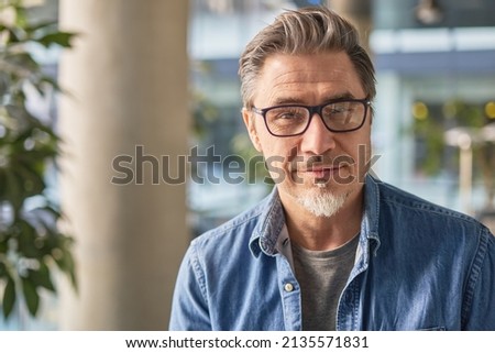Portrait of happy middle aged man in glasses, standing in office lobby wearing casual shirt. Royalty-Free Stock Photo #2135571831