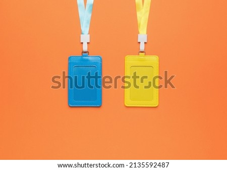 Yellow and blue badges on ribbons on an orange background. Name badge. A device for cards and business cards. Flat lay.