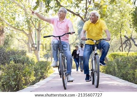 Two cheerful senior men having fun riding bicycle at park
