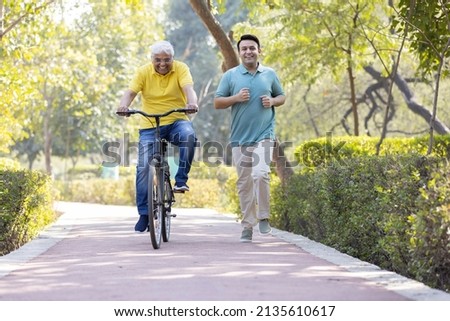 Cheerful senior man riding bicycle  while son running at park
 Royalty-Free Stock Photo #2135610617