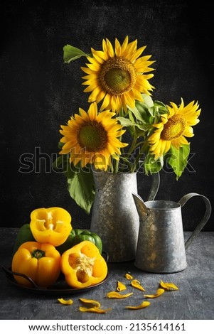Beautiful sunflowers are placed in a vase, around them are green and yellow peppers. Selective focus