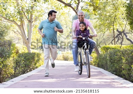 Old man riding bicycle with granddaughter while son running at park
 Royalty-Free Stock Photo #2135618115