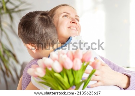 A cute son giving his mother a bouquet of tulips congratulating her on mother's day while celebrating the holiday at home.